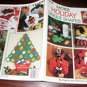 May include: A magazine spread showcasing various holiday-themed plastic canvas crafts. Featured items include a Christmas tree with ornaments, a heart-shaped basket, a pumpkin, a turkey, and a candle. The text reads "MORE HOLIDAY UNIQUE SHAPES".