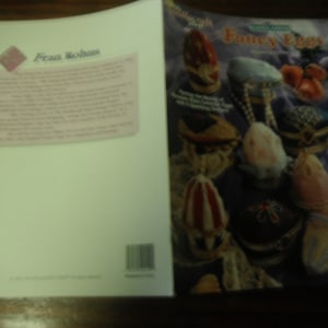 May include: A book titled "Fancy Eggs" with various decorated egg designs on the cover. The book is open, revealing a blank page with text and a pink diamond-shaped logo. The cover features a variety of colorful, decorative eggs.