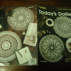 May include: Two open booklets featuring white crocheted doily patterns. One booklet is titled "Today's Doilies" and the other features the word "Tarantella". The cover of "Today's Doilies" shows several doily designs.