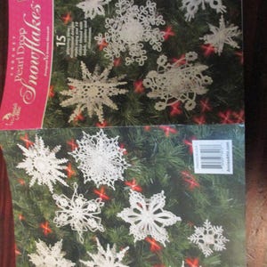May include: A craft pattern book titled Pearl Drop Snowflakes by Annie's Attic featuring 15 crocheted white snowflake designs. The cover displays various intricate white snowflake ornaments against a green pine background with red lights.