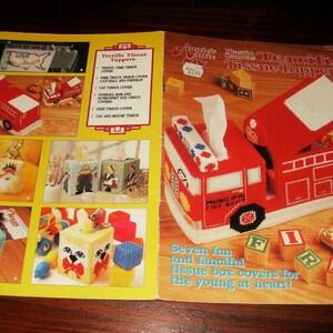 May include: A magazine cover featuring various tissue box covers. The main image showcases a red fire truck tissue box cover with the words "Municipal Fire Dept." The cover also displays other designs, including a cat, a fish, and a travel-themed cover.