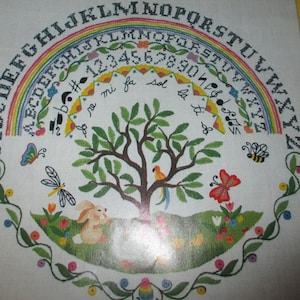 May include: Cross-stitch sampler featuring a rainbow arch with the alphabet and numbers. Below the arch is a tree with a parrot, a bunny, and butterflies. The design is framed by a floral border, creating a colorful and whimsical scene.
