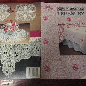 May include: A craft instruction book titled New Pineapple Treasury by Rita Weiss, featuring white crocheted doilies and tablecloths with pineapple patterns, alongside a pink crocheted bedspread with floral accents and a barcode on the back.