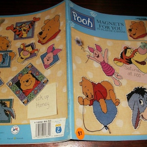 May include: A craft instruction booklet titled Pooh Magnets For You In Plastic Canvas featuring various Winnie the Pooh character designs including Tigger, Piglet, and Eeyore. The cover displays finished plastic canvas projects and notes.