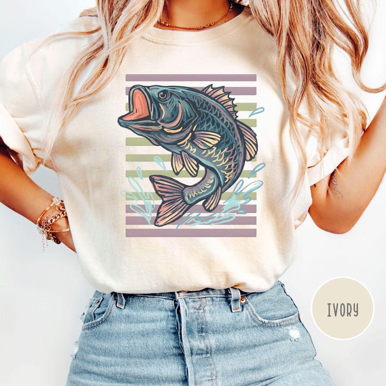 May include: Ivory t-shirt with a detailed illustration of a fish leaping from water. The fish is in shades of blue, purple, and yellow, set against a striped background of purple and green. The word "IVORY" is printed on the bottom right.