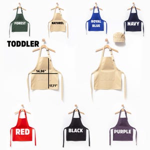 May include: A set of ten toddler-sized aprons in various colors, including forest green, natural, royal blue, navy, red, black, and purple. The aprons are hanging on hangers and have adjustable straps. The aprons are 14.96 inches wide and 17.71 inches long. The set also includes a white chef's hat.