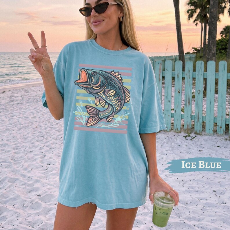 May include: Light blue t-shirt with a fish graphic and horizontal stripes. The fish is depicted with an open mouth. The shirt is short-sleeved and the text "Ice Blue" is printed on the bottom right. The shirt is a light blue colour.