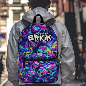 May include: A backpack with a vibrant skull pattern in shades of purple, blue, yellow, and pink. The word "ERICK" is displayed in white block letters. The backpack has a black handle and straps.
