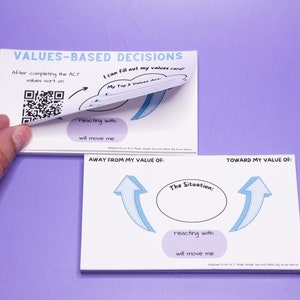 May include: Two white cards with blue and black text and illustrations. The top card has the text "VALUES-BASED DECISIONS" and a QR code. The bottom card has the text "AWAY FROM MY VALUE OF:" and "TOWARD MY VALUE OF:" with arrows pointing up.
