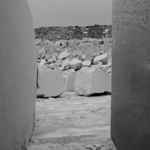 May include: A black and white photograph of a quarry with large blocks of stone. The blocks are stacked in a pile and there is a gap between two of the blocks.