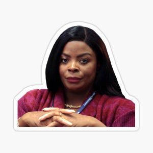 May include: A woman with dark hair and a serious expression is wearing a red shirt and a blue lanyard with the text "Lemonade Day" on it. She is sitting with her hands clasped in front of her.