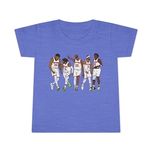 Op de afbeelding: Een blauw peuter-T-shirt met een afbeelding van vijf basketballers in witte uniformen met oranje accenten. De spelers staan in verschillende poses, met één die zijn hand opsteekt. De tekst "NEW YORK" is zichtbaar op de uniformen.