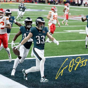May include: A football game in progress, featuring players in green and white uniforms, and red and white uniforms. The players are running on a green field. The image includes a signature in yellow.