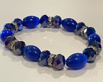 May include: A blue beaded bracelet with a mix of oval and faceted beads. The bracelet features a combination of deep blue and iridescent beads, with silver-toned accents. This stretch bracelet is a piece of jewelry.