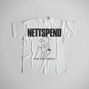 May include: White t-shirt with the word "NETTSPEND" in bold black letters across the chest. Below the text is a black and white cartoon drawing of a creature holding a cup. The phrase "I DON'T WANT TO GROW UP" is printed below the drawing.