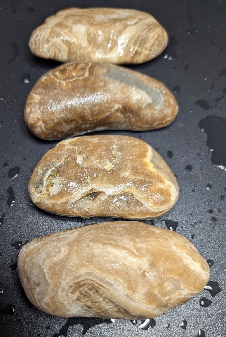 Puede incluir: Cuatro piedras lisas de forma ovalada en tonos marrones y beige. Las piedras tienen un aspecto pulido, con patrones y texturas visibles. La disposici&oacute;n es vertical, con las piedras ligeramente superpuestas.