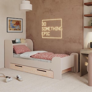 Puede incluir: Una habitación moderna con una cama rosa claro, ropa de cama con estampado rojo y un letrero de neón que dice "DO SOMETHING EPIC". La habitación también incluye un escritorio, una silla y una pequeña mesita de noche. La cama tiene un cajón.