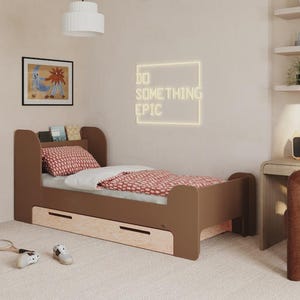 Op de afbeelding: Een bruin bed met een rood patroon dekbed en kussen, in een kinderkamer. Het bed heeft een ingebouwde boekenplank en opberglades. Een neonbord leest "DO SOMETHING EPIC". Een bureau en stoel staan ook in de kamer.