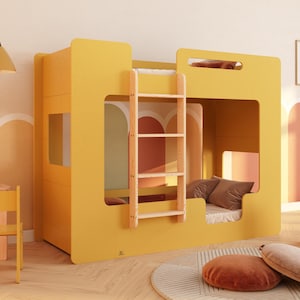 Op de afbeelding: Een heldergeel stapelbed met een houten ladder. Het bed heeft een vierkant ontwerp met uitgesneden ramen en een gezellig interieur. De kamer heeft een klein bureau, een stoel en decoratieve lampen. De vloer heeft een rond tapijt en twee kussens.