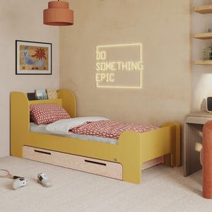 Puede incluir: Una cama amarilla mostaza con un edredón y una almohada estampados en rojo. La habitación incluye un escritorio, una silla y un letrero de neón que dice "DO SOMETHING EPIC". La cama tiene una estantería incorporada y dos cajones.