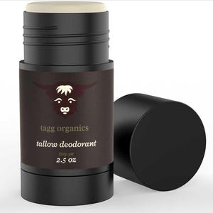 Op de afbeelding: Een zwarte deodorantstick met een lichtbeige bovenkant en een losse zwarte dop. Het etiket toont een stierenlogo en de tekst "tagg organics tallow deodorant Holy-pit 2.5 OZ".