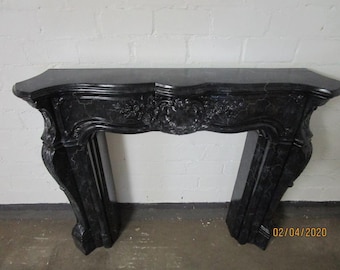 Könnte beinhalten: Schwarzer Marmor-Kaminmantel mit Ziergravuren. Der Kamin hat eine geschwungene Oberseite und dekorative Blumen- und Schnörkeldetails. Die Beine sind abgewinkelt. Ein Datumsstempel vom 02.04.2020 ist auf dem rechten Bein sichtbar.