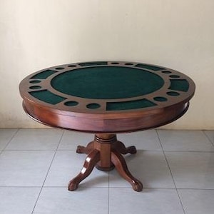 Op de afbeelding: Een ronde houten pokertafel met een donkergroen vilten speeloppervlak. De tafel heeft een donkerbruine afwerking en individuele spelersposities. Hij staat op een voetstuk met klauwpoten.