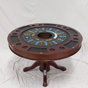 Op de afbeelding: Een ronde casinotafel in mahoniekleur, met een zwart vilten speeloppervlak. De tafel heeft een roulette-wielontwerp met nummers en inzetgebieden. Het heeft een voetstuk met klauwpoten.