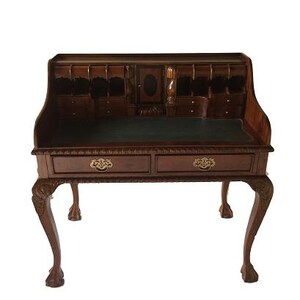 Peut inclure: Un bureau en bois de style ancien avec un plan de travail vert foncé. Le bureau comporte deux tiroirs avec des poignées en laiton et des pieds incurvés. La partie supérieure comprend de petits tiroirs et compartiments, et une armoire centrale.