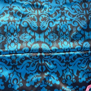 May include: Close-up of a fabric with a repeating damask pattern. The design features a vibrant teal blue against a dark charcoal background. The fabric has a silky sheen, suggesting a luxurious material.