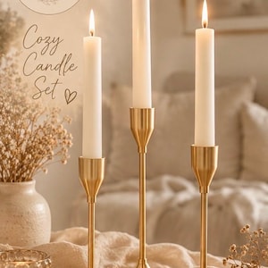 Könnte beinhalten: Drei hohe, schlanke Kerzenhalter aus goldfarbenem Metall mit glatter Oberfläche, die jeweils eine einzelne weiße Stabkerze mit brennender Flamme tragen. Der Text NOLIA HOME DESIGN und Cozy Candle Set ist oben links im Bild zu sehen.