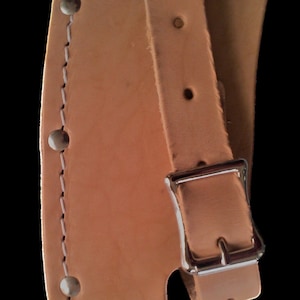 May include: A tan leather axe sheath with a white stitched border and a silver buckle. The sheath has a belt loop and is designed to hold an axe securely.