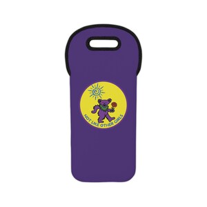 May include: A purple wine bottle carrier with a black handle. A yellow circle features a purple bear holding a flower, with a sun graphic and the text "NOT LIKE OTHER GIRLS".