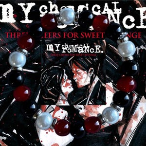 May include: A beaded bracelet featuring black, red, and white beads. The bracelet is set against a dark background with the text "MY CHEMICAL ROMANCE" and "THREE CHEERS FOR SWEET REVENGE".