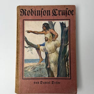 Könnte beinhalten: Ein Vintage-Buch mit dem Titel "Robinson Crusoe" und einer Illustration von zwei Figuren auf dem Cover. Das Cover ist rotbraun mit dem Titel in verzierten schwarzen Buchstaben. Die Illustration zeigt einen Mann, der zeigt, mit einem anderen Mann unter ihm.