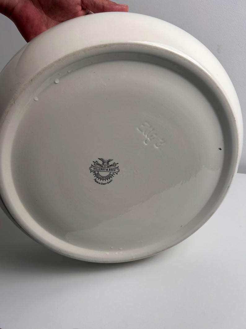 May include: A white ceramic bowl base featuring a black printed Villeroy & Boch logo with an eagle emblem and the text Made in Saar-Basin. The underside also includes an embossed mark with the characters 2KG 3 on the smooth, glazed surface.