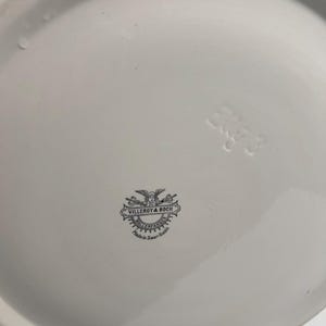 May include: The underside of a white ceramic plate featuring a black printed Villeroy & Boch logo with a winged figure and the text Wallerfangen Made in Saar-Basin. An embossed number 3 is visible on the smooth, glossy white surface.