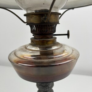 May include: An antique oil lamp with a clear glass globe and a metal base. The lamp features a brass burner and a glass shade. The base has a decorative, ornate design. The lamp is designed to be placed on a table or other surface.