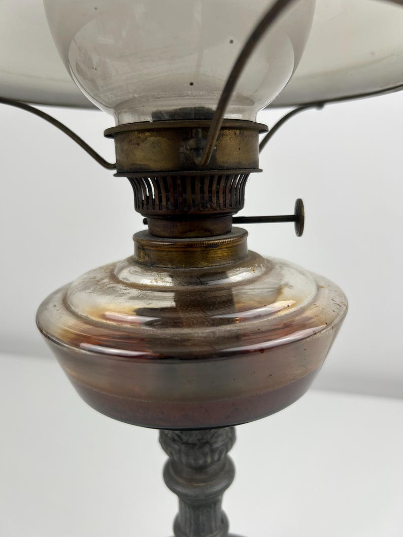 May include: An antique oil lamp with a clear glass globe and a metal base. The lamp features a brass burner and a glass shade. The base has a decorative, ornate design. The lamp is designed to be placed on a table or other surface.