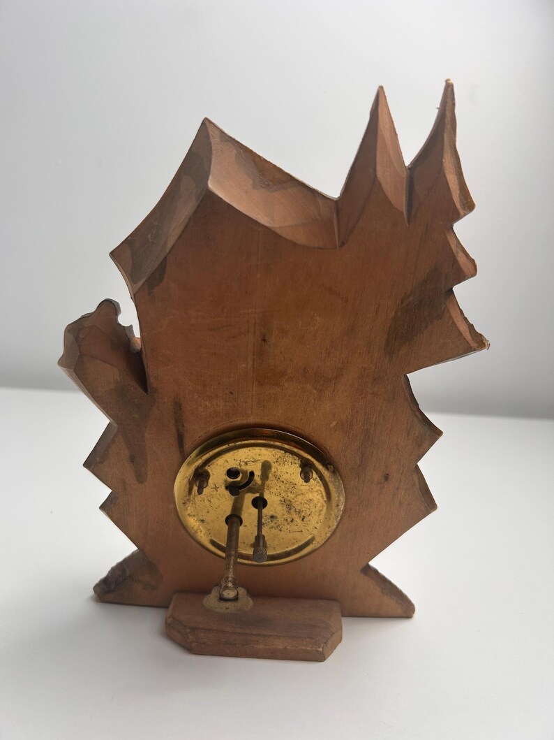 May include: A light brown wooden clock back featuring an irregular, jagged silhouette resembling a mountain or tree shape. A circular brass mechanism is mounted in the center, displaying two thin metal adjustment stems extending outward.