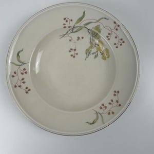 Könnte beinhalten: Eine weiße Suppenschüssel aus Keramik mit goldfarbenem Rand und einem floralen Design in Grün-, Braun- und Gelbtönen.