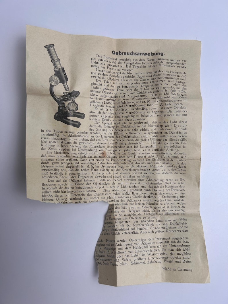K&ouml;nnte beinhalten: Eine alte, cremefarbene Bedienungsanleitung aus Papier mit einer schwarz-wei&szlig;en Strichzeichnung eines Mikroskops auf der linken Seite. Das Dokument enth&auml;lt umfangreichen deutschen Text mit dem Titel Gebrauchsanweisung und endet mit Made in Germany.