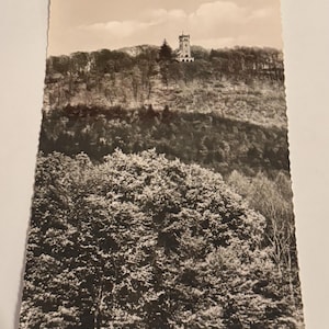 Könnte beinhalten: Vintage Schwarz-Weiß-Postkarte mit einem Turm auf einem bewaldeten Hügel. Der Turm hat ein detailliertes Design. Der Vordergrund ist mit dichtem Laub gefüllt. Der Text "Rinteln/Weser-Klippenturm" ist unten auf der Karte aufgedruckt.