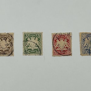Könnte beinhalten: Vier alte bayerische Briefmarken. Die quadratischen Marken mit verzierten Rändern weisen verschiedene Werte und Farben auf: Braun, Grün, Rot und Blau. Jede Marke hat deutschen Text.