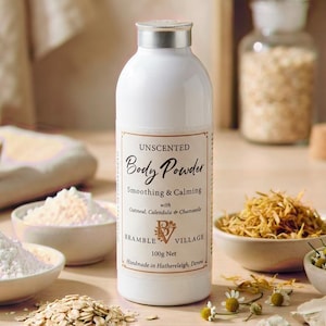 May include: White unscented body powder bottle with a silver lid. The label reads "Body Powder, Smoothing & Calming" with oatmeal, calendula, and chamomile. Bowls of powder, oats, and dried flowers surround the bottle. The net weight is 100g.