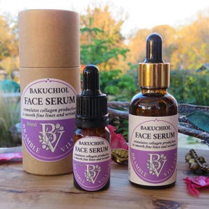 May include: Two brown glass bottles of Bakuchiol Face Serum with black droppers and gold accents, and a cylindrical cardboard container. The labels are white with purple accents and text. The serum is designed to stimulate collagen production.