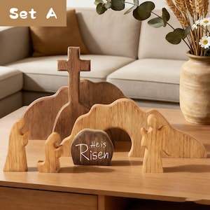 May include: Wooden Easter scene set with a cross, figures, and a tomb with the text "He is Risen." The set includes a cross, figures, and a tomb, all crafted from wood. The scene is set on a wooden table, with a neutral background.