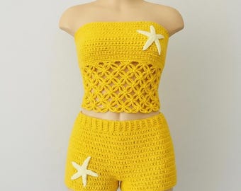May include: A bright yellow two-piece crochet set consisting of a strapless tube top and matching shorts. The top features a central section with an openwork floral pattern and a white starfish appliqué. The shorts also feature a white starfish.