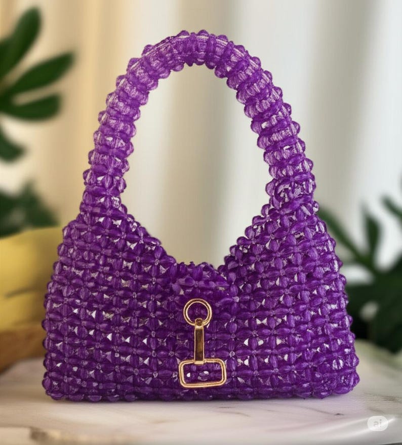 May include: A handcrafted, purple beaded handbag with a structured design. The bag features a rounded handle and a gold-colored clasp. The beads are arranged in a geometric pattern, creating a textured surface. The bag is designed to be carried by hand.
