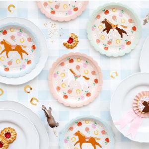 Pode incluir: Um conjunto de pratos de papel rosa pastel e azul com um design de cavalo e ferradura. Os pratos têm uma borda festonada e são perfeitos para uma festa infantil.